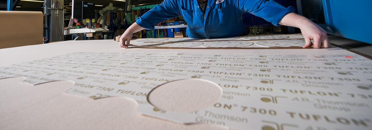 A man cutting a large sheet of Tuflon Gasket material
